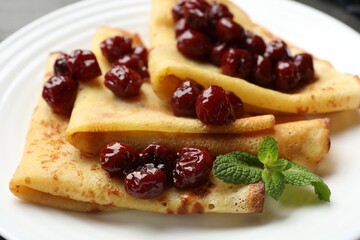 Tasty crepes with cherries and mint on table, closeup