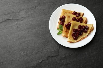Tasty crepes with cherries and mint on black table, top view. Space for text