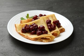 Tasty crepes with cherries and mint on black table, closeup