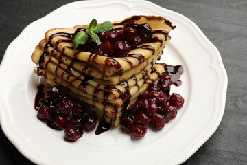 Tasty crepes with cherries, chocolate and mint on black table, closeup