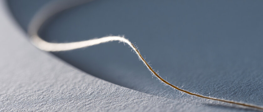 Close-up of a single thin thread casting a shadow on textured paper with soft natural lighting and shallow depth of field