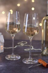 Glasses of white wine and Christmas decor on grey table against background with blurred lights