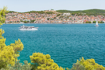 The coastal town of &Scaron;ibenik in Croatia sits on the seafront, with hilltop houses, the Barone Fortress, and St. Michael's Castle. View from the other side on a sunny summer day.