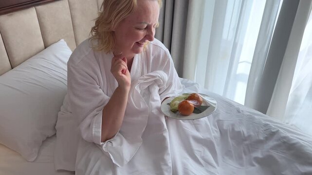 tangerines banana hotel compliment woman bed, showcasing a mix of tableware and dishware. The plate she holds has a delicious cuisine dish, ready to be shared, breakfast in bed. 