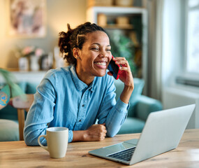 Portrait of a young black woman using a smartphone and laptop at home office