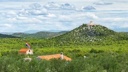 Croatian landscape with green hills and a Catholic church on top of a mountain, view from a bike...
