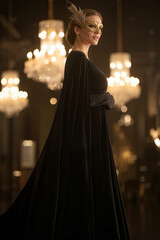 Elegant woman in a flowing black gown and feathered mask stands gracefully in a luxurious setting, surrounded by sparkling chandeliers, embodying a sense of mystery and sophistication