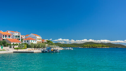 Obraz premium The seaside town of Jezera in Croatia, a small bay with hills above the blue water, view from the bay over the water on a sunny summer day.