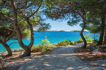 A natural rocky coastline with clear blue waters. A view from the coastal path to distant green islands on a sunny day.