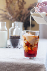 Pouring milk into a glass with cold brew coffee and ice.