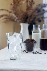 A clear glass of ice sits on a table covered with a linen tablecloth.