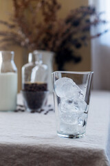 A clear glass of ice sits on a table covered with a linen tablecloth.