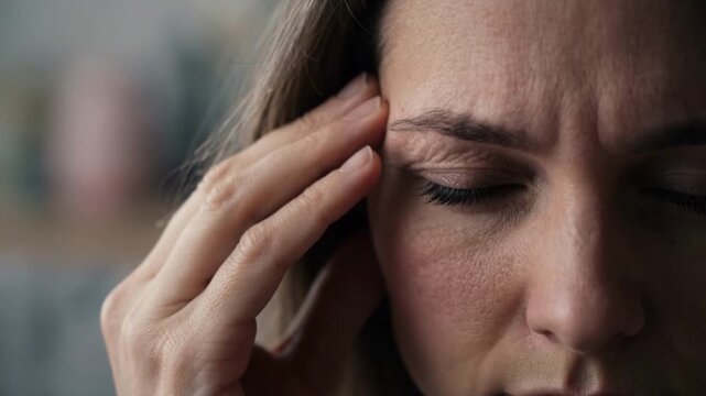 A woman suffering from a severe headache. Close-up of a person in pain touching their temple. Migraine and stress concept