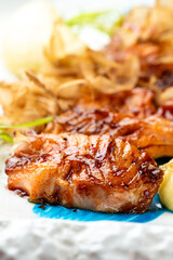 Close-up of a glossy, glazed grilled salmon fillet served with crispy garnish and fresh herbs on a vibrant blue and white patterned plate, an appetizing mea