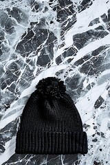 Black knitted winter hat with pompom rests on a textured surface of white and dark gray stone