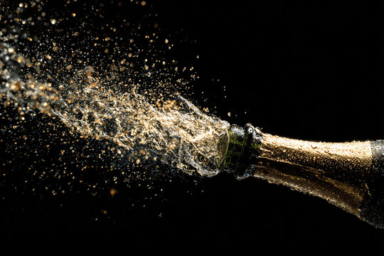 High-speed capture of champagne bottle opening, exploding bubbles, droplets sparkling in golden light, black background