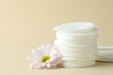 Stack of clean cotton pads and flower on beige background, closeup. Space for text