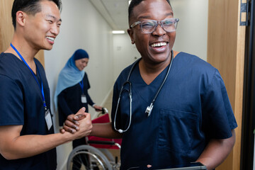 Diverse staff standing in hospital, navy-clad holding tablet, hijab-clad guiding wheelchair
