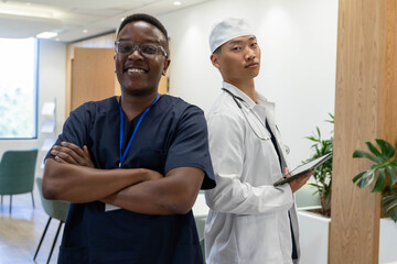 Diverse male staff standing in reception, wearing scrubs and coat, holding tablet and stethoscope