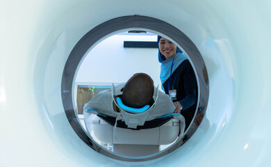 African American woman patient lying with blue head pad entering CT gantry while woman tech guiding