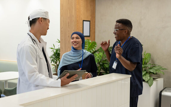 Diverse clinic staff using tablet and discussing intake at reception with stethoscope, lanyard ID