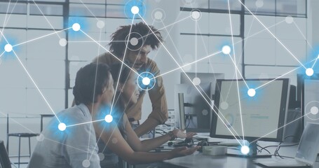 Working three coworkers in casual tops leaning in office, pointing at monitors and network overlay © vectorfusionart