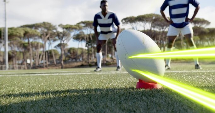 Balancing white rugby ball on red tee on grass pitch, neon streaks, players wearing striped jerseys - Powered by Adobe