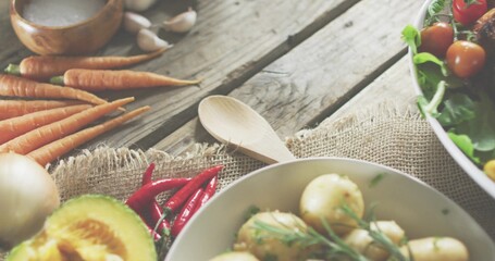 Displaying bowl of boiled potatoes with herbs on wooden table, with wooden spoon, carrots, avocado © vectorfusionart