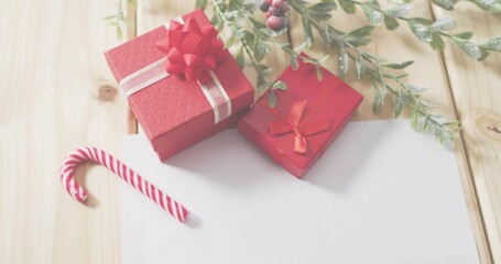 Displaying two red gift boxes with ribbons on light wooden table, candy cane and foliage