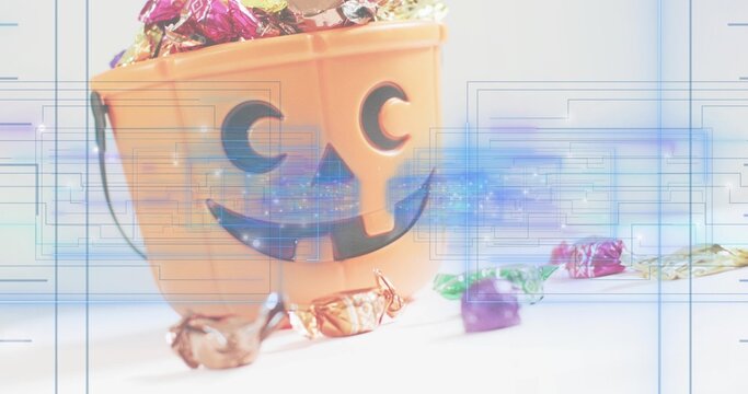 Sitting orange jack-o-lantern bucket holding foil candies on white tabletop, with digital overlays