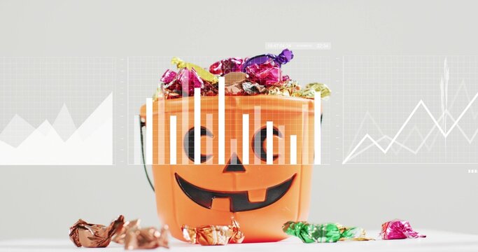 Showing orange jack-o'-lantern bucket filled with foil candies on white table, graph overlays - Powered by Adobe