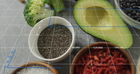 Showing white bowl of chia-like seeds on gray countertop, halved avocado, broccoli, goji, grid
