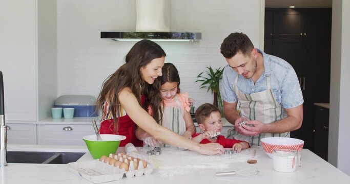 Baking family of four preparing dough at home kitchen island, using cookie cutters, wearing aprons