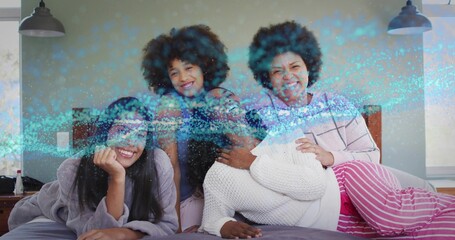 Reclining four women wearing pajamas and loungewear on bed in bedroom, with blue overlay