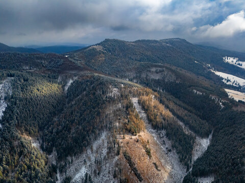 Aerial view of sunlit mountain ridges and snow-dusted forests create a captivating contrast under a cloudy sky in Svatodusna dolina valley, Lubietova, Banska Bystrica Region, Slovakia.