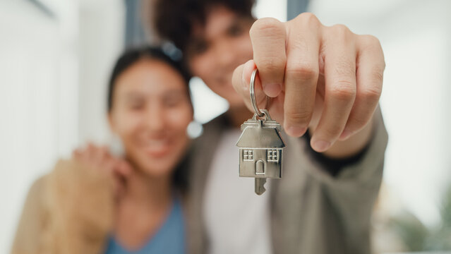 Close-up Young happy Asian sweet couple hug each other smiling looking at camera so proud show off new house keychain in living room. Husband wife move new home, Apartment Rent And Ownership Concept.
