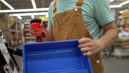 Professional builder wearing brown overalls and light green t-shirt uses barcode scanner to scan...
