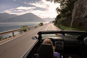 Young woman driving convertible along scenic ocean coast and mountain road at sunset, carefree...