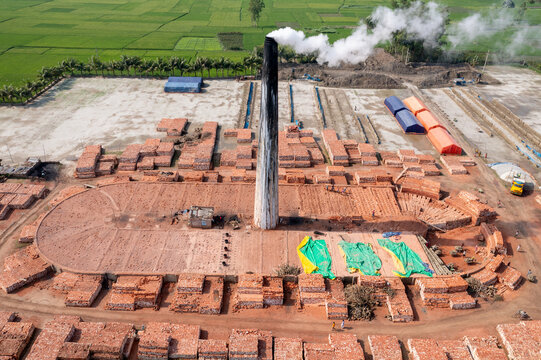 Aerial view of a brick factory with a tall chimney billowing smoke into the sky, surrounded by patterns of red bricks, Bogura, Rajshahi Division, Bangladesh.