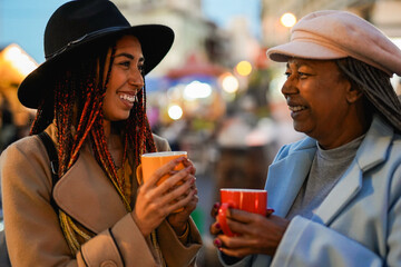 Happy african mother and daughter drinking hot chocolate at Christmas street market - Winter holiday, travel and family lifestyle
