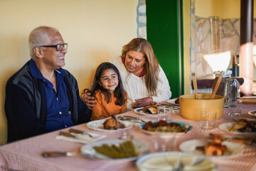 Happy latin female child having fun during lunch with grandparents at home patio - Family, love and winter holiday concept