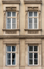 Obraz premium Historic building facade with ornate classical window frames, decorative stucco elements and symmetrical architectural details in warm beige tones