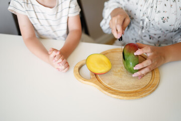 Mother slicing fresh mango for a child’s healthy snack at home, showing clean food preparation and family nutrition.