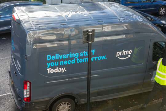 London. UK- November 23.2025. A street view of an Amazon delivery vehicle with the Prime symbol and logo on the side, and the driver making home deliveries to customers.