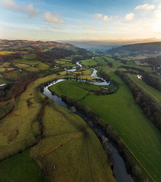 Aerial view of the winding River Dee s snaking through verdant fields and rolling hills under a soft, golden sky, Bala, Wales, United Kingdom.