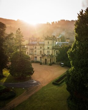 Aerial view of a majestic building bathed in the warm glow of the rising sun, nestled amidst lush green trees and manicured gardens, Bala, Wales, United Kingdom.