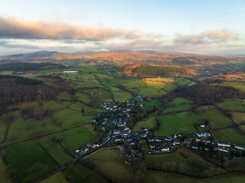 Aerial view of a green and textured landscape with small clusters of buildings nestled within the rolling hills under a soft, pastel sky, Bala, Wales, United Kingdom.