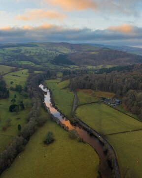 Aerial view of the River Dee snaking through the green fields and rolling hills, reflecting the soft, golden hues of the setting sun, Bala, Wales, United Kingdom.