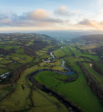 Aerial view of a vibrant green valley carved by a winding river under a soft, cloudy sky, Bala, Wales, United Kingdom.