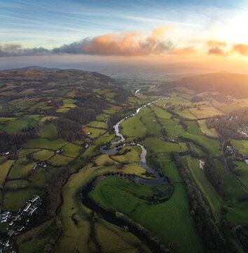 Aerial view of a winding river snaking through verdant fields, a tapestry of green and gold under a pastel sky, Bala, Wales, United Kingdom.